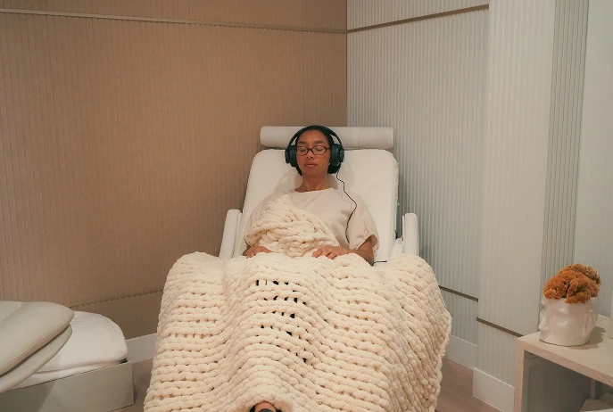A patient resting in a treatment chair under a knit blanket, wearing headphones, during a session at Mystic Health